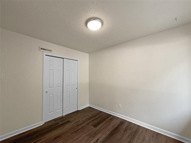 unfurnished bedroom with a textured ceiling, dark wood-type flooring, and a closet