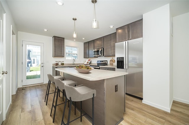 kitchen featuring dark brown cabinetry, stainless steel appliances, decorative light fixtures, light hardwood / wood-style flooring, and a center island