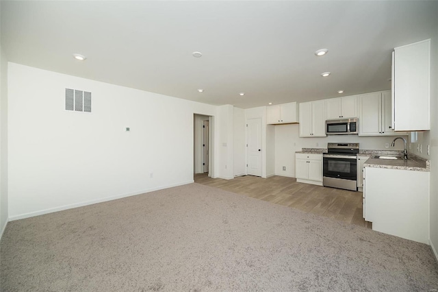 kitchen with light stone countertops, light carpet, stainless steel appliances, sink, and white cabinetry