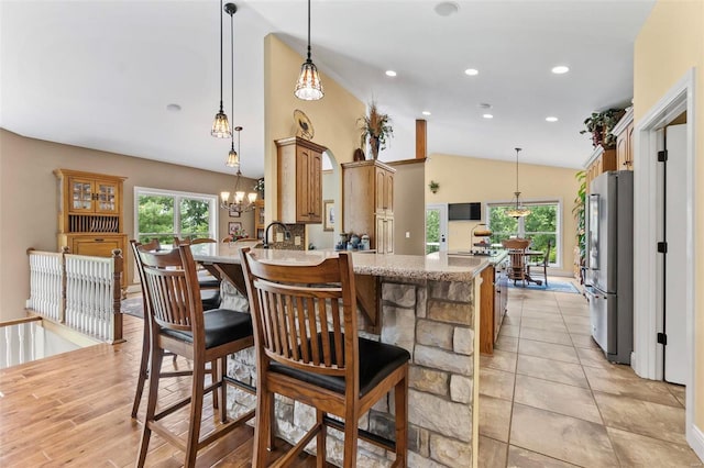 kitchen featuring light stone counters, vaulted ceiling, light hardwood / wood-style floors, stainless steel refrigerator, and kitchen peninsula