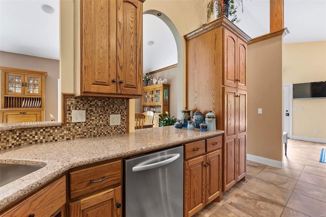 kitchen featuring stainless steel dishwasher, light tile patterned floors, light stone counters, and backsplash