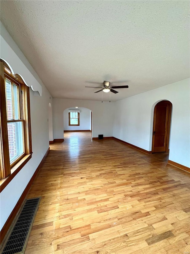 unfurnished living room with visible vents, arched walkways, baseboards, light wood-style flooring, and a textured ceiling