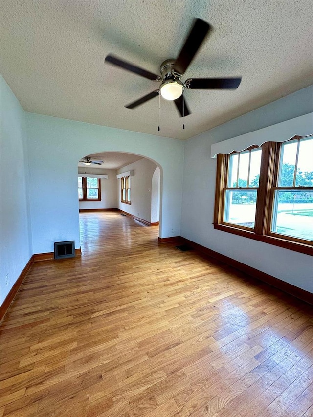 unfurnished room featuring arched walkways, light wood-style flooring, visible vents, and baseboards