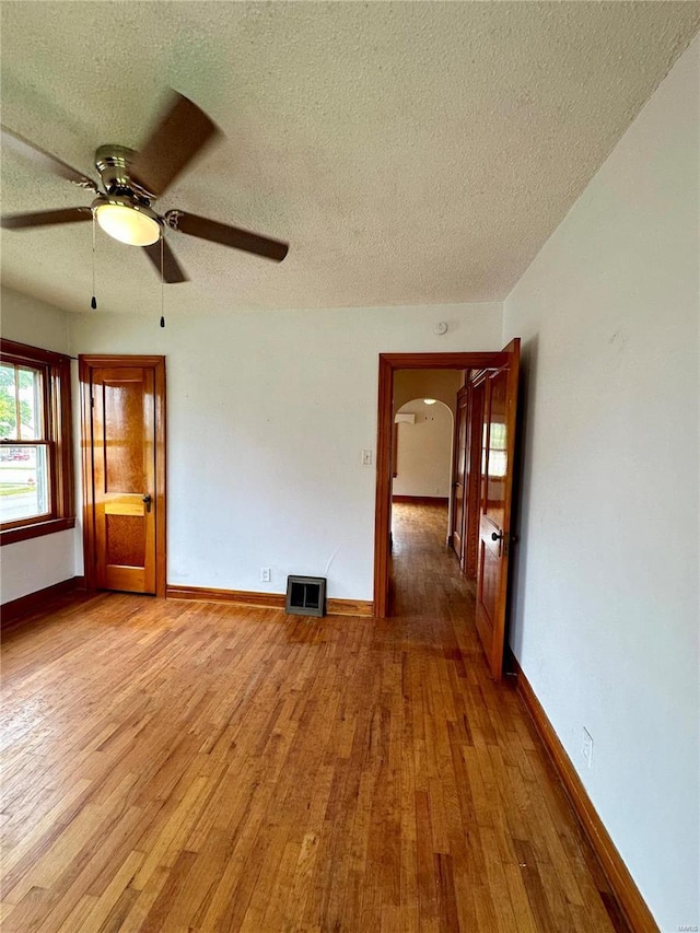 empty room featuring arched walkways, a textured ceiling, baseboards, and wood finished floors