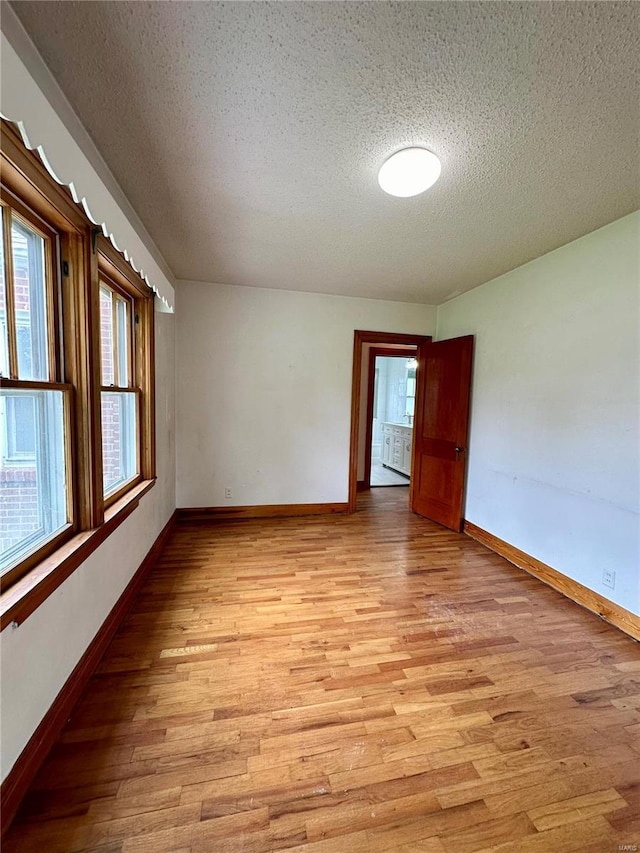 empty room featuring light wood-style flooring, baseboards, and a textured ceiling