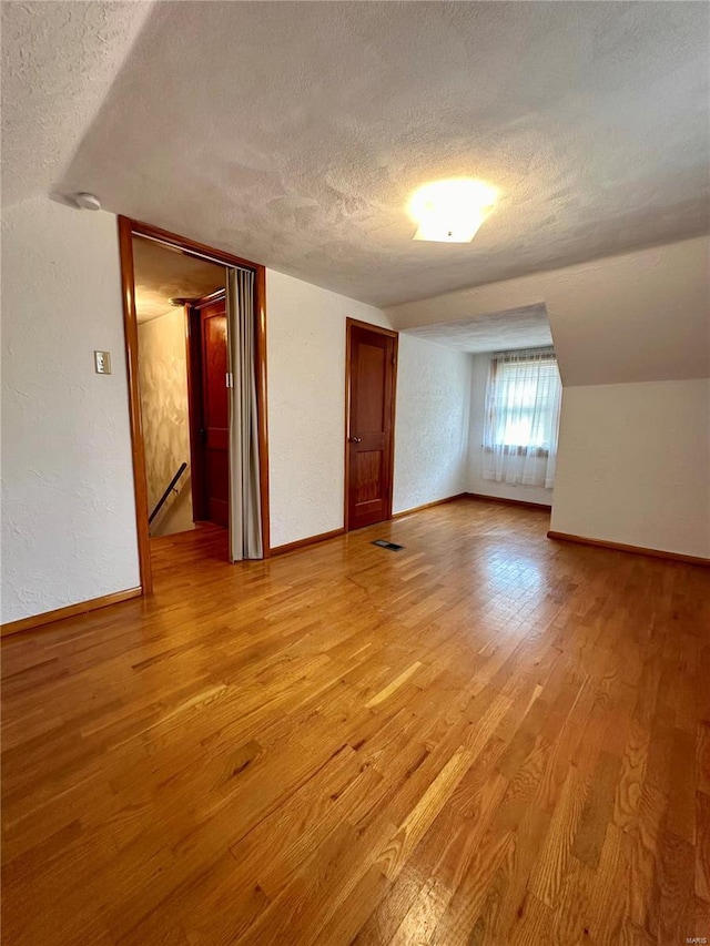 additional living space featuring baseboards, a textured wall, a textured ceiling, and light wood finished floors