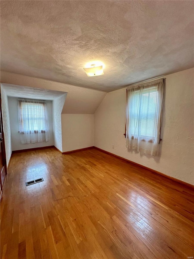 bonus room with light wood finished floors, lofted ceiling, visible vents, a textured wall, and a textured ceiling