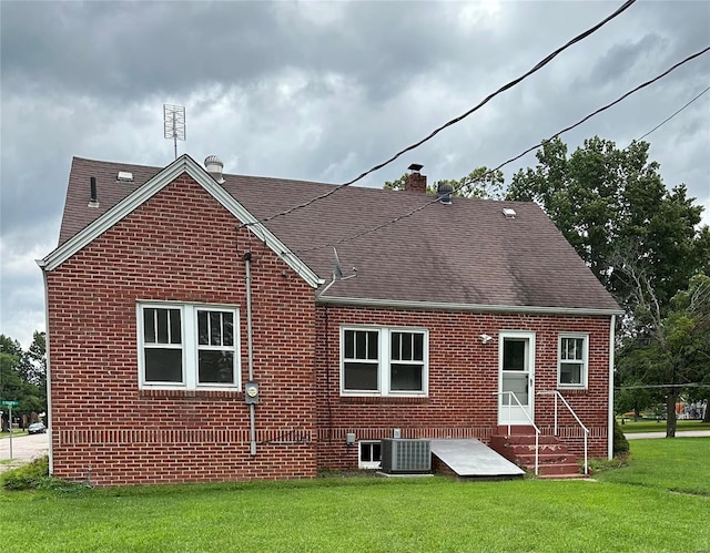 back of house featuring brick siding, a lawn, a chimney, and central AC unit