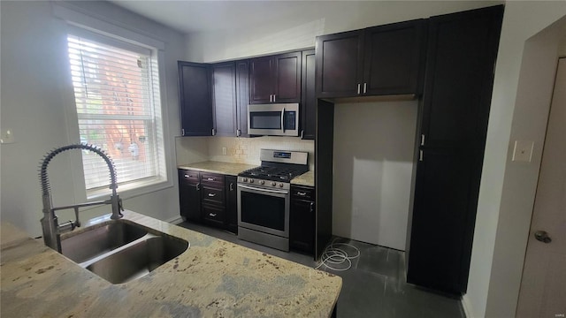 kitchen with a wealth of natural light, light stone counters, appliances with stainless steel finishes, and sink