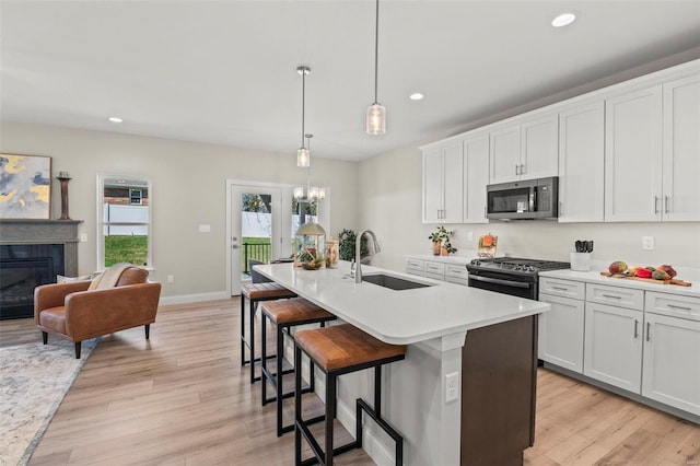 kitchen with appliances with stainless steel finishes, decorative light fixtures, white cabinetry, an island with sink, and sink