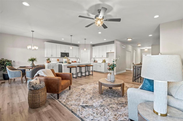 living room with ceiling fan with notable chandelier and light hardwood / wood-style flooring