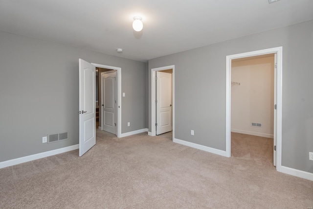 unfurnished bedroom with light colored carpet, a closet, and a walk in closet