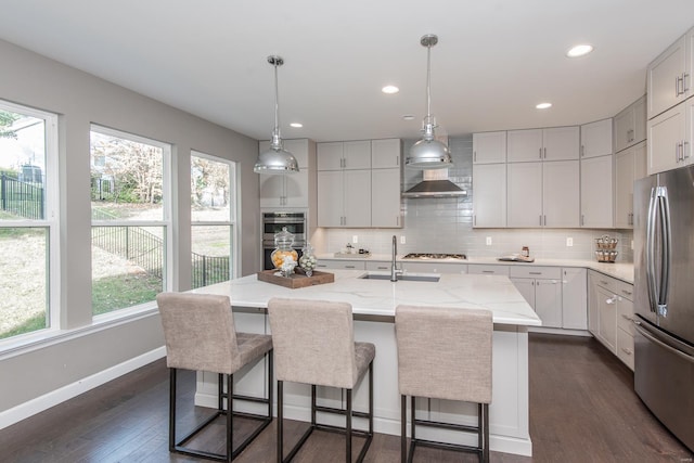 kitchen featuring dark wood-type flooring, an island with sink, stainless steel appliances, decorative light fixtures, and white cabinetry