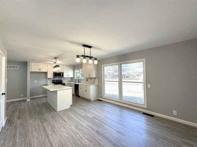 kitchen featuring stainless steel appliances, sink, hanging light fixtures, light hardwood / wood-style floors, and white cabinetry