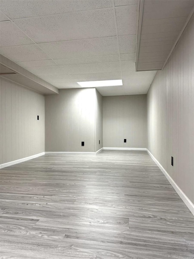 basement featuring wood walls, wood-type flooring, and a drop ceiling