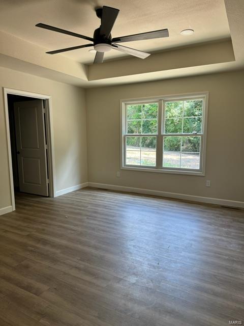 unfurnished room with baseboards, a raised ceiling, and dark wood-style flooring