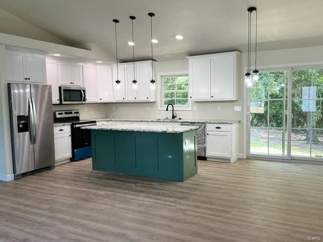 kitchen with white cabinets, stainless steel appliances, decorative light fixtures, and light hardwood / wood-style floors