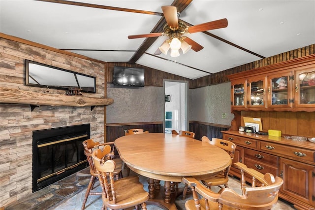 dining room featuring wood walls, a fireplace, ceiling fan, and vaulted ceiling