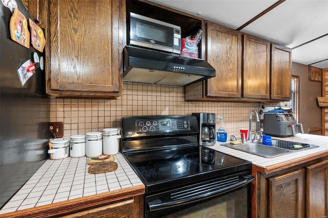 kitchen with backsplash, tile counters, wall chimney exhaust hood, and black range with electric stovetop