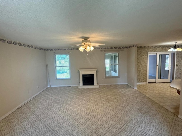 unfurnished living room featuring ceiling fan with notable chandelier and a textured ceiling