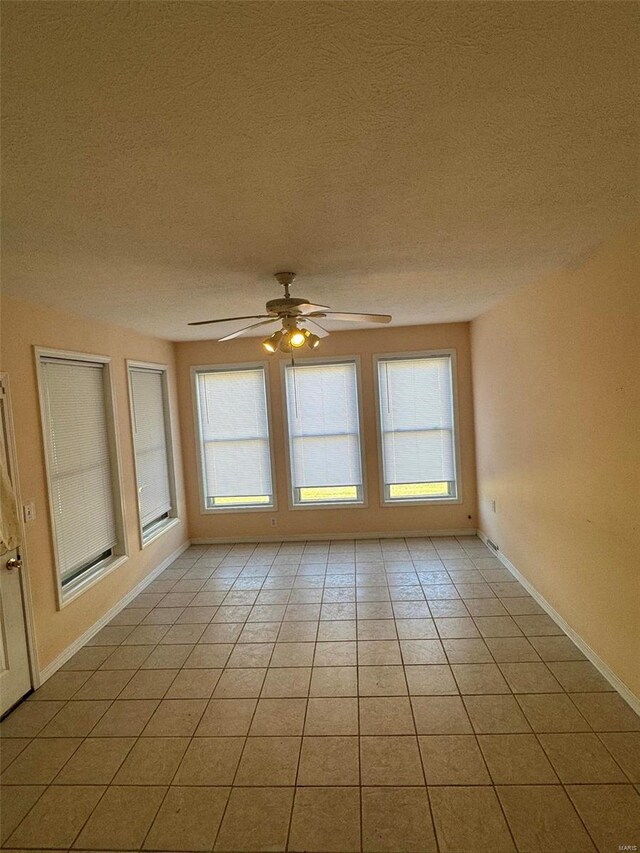 empty room with a textured ceiling, light tile patterned floors, and ceiling fan