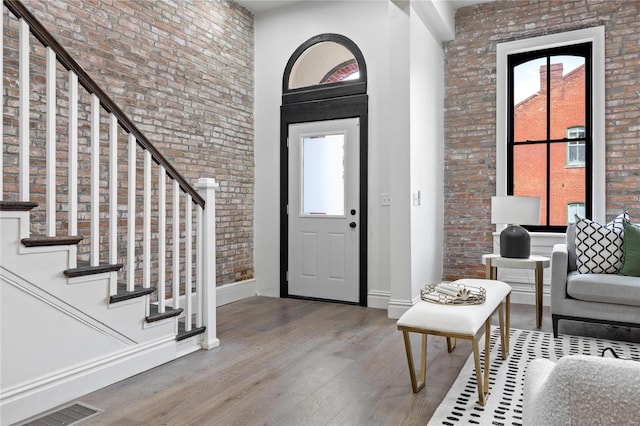 foyer featuring a healthy amount of sunlight, wood-type flooring, and brick wall