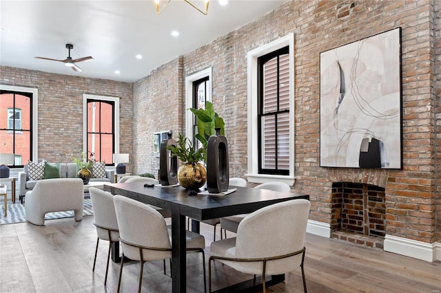 dining space featuring brick wall, a fireplace, light wood-type flooring, and a healthy amount of sunlight