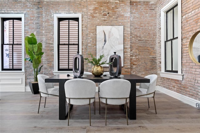 dining area featuring brick wall, wood-type flooring, and plenty of natural light