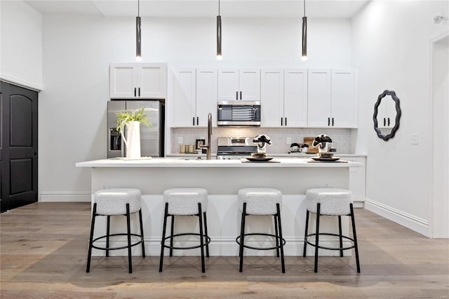 kitchen featuring stainless steel appliances, a center island with sink, pendant lighting, white cabinets, and light hardwood / wood-style floors