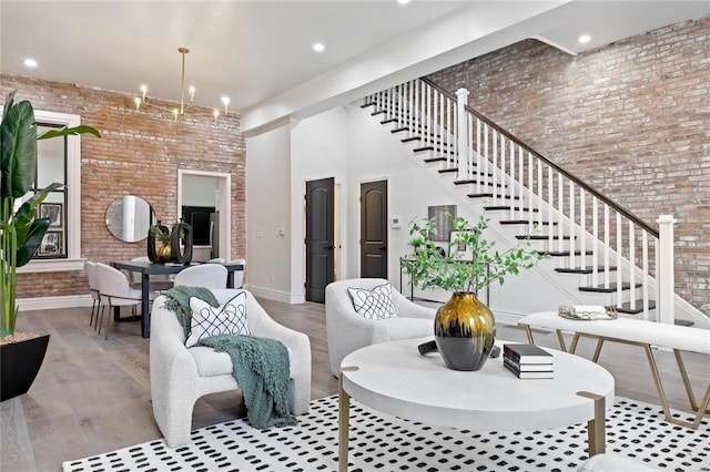 living room featuring light hardwood / wood-style floors, brick wall, a towering ceiling, and an inviting chandelier