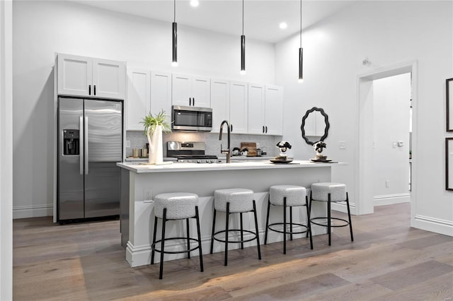 kitchen featuring white cabinetry, appliances with stainless steel finishes, pendant lighting, and a kitchen island with sink