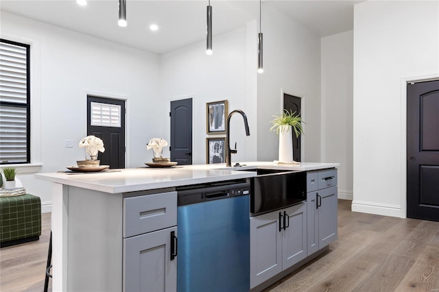 kitchen with stainless steel dishwasher, an island with sink, light hardwood / wood-style floors, and gray cabinets