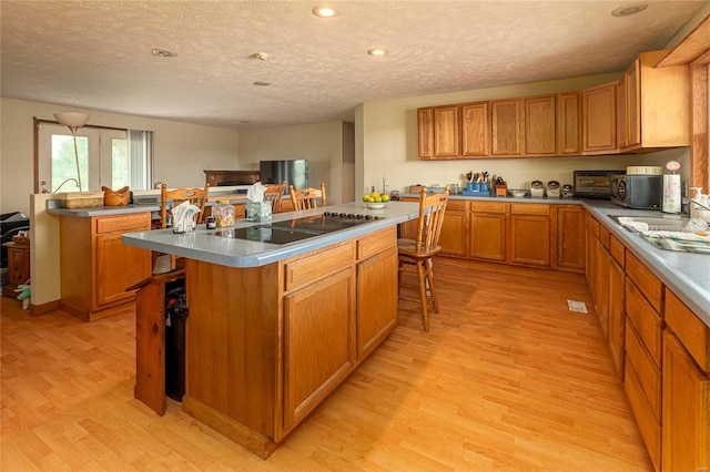 kitchen with light wood-type flooring, black electric stovetop, a textured ceiling, a kitchen bar, and a kitchen island