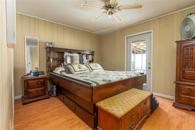 bedroom featuring ceiling fan, access to outside, a textured ceiling, wooden walls, and light hardwood / wood-style floors