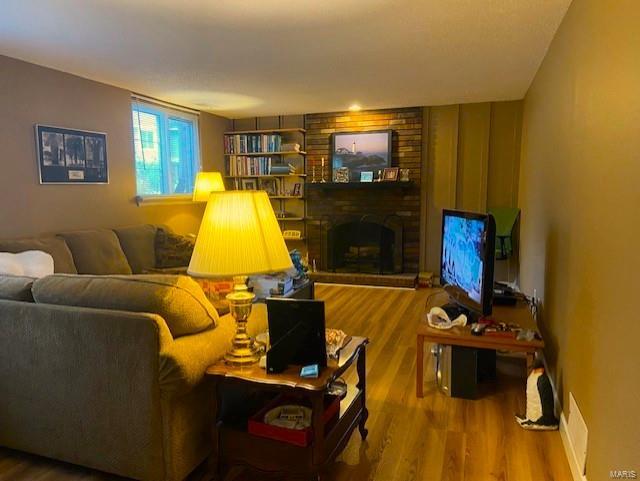 living room featuring a fireplace, hardwood / wood-style floors, and brick wall