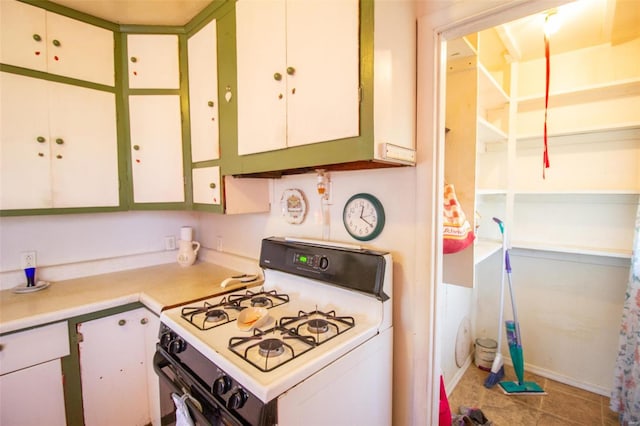 kitchen with white range with gas stovetop, white cabinetry, and light tile patterned flooring