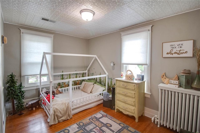 bedroom with radiator heating unit, multiple windows, and wood-type flooring