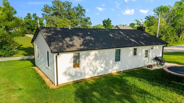 rear view of property with a yard and a trampoline