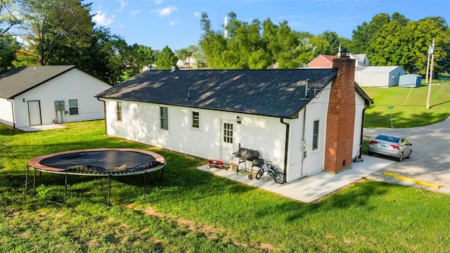 rear view of house with a trampoline, a patio, and a yard