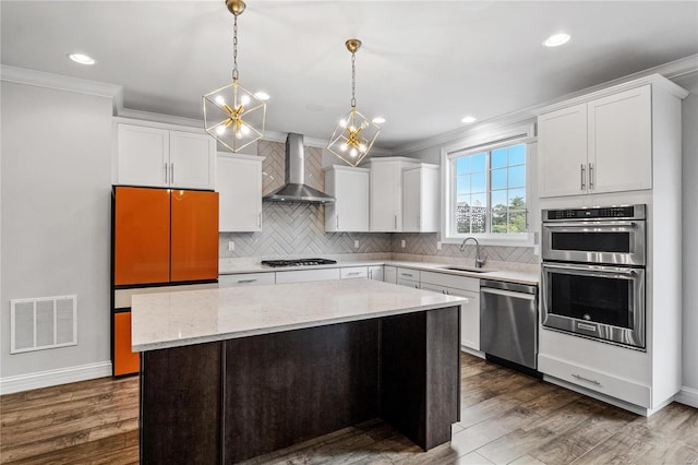 kitchen with a sink, visible vents, white cabinets, appliances with stainless steel finishes, and wall chimney exhaust hood