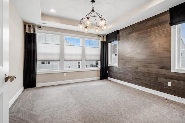 carpeted spare room featuring wood walls, baseboards, a raised ceiling, and a chandelier