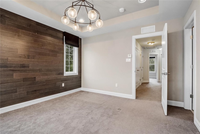 spare room featuring wooden walls, light carpet, an accent wall, visible vents, and a raised ceiling