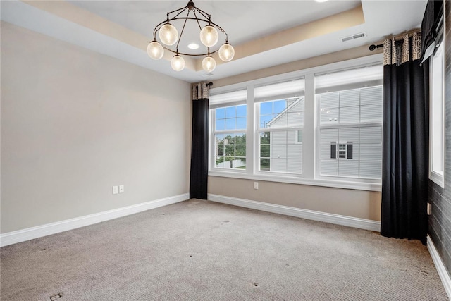 carpeted empty room with a chandelier, a raised ceiling, visible vents, and baseboards