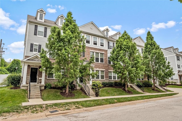 view of property featuring a front yard, brick siding, and stairs