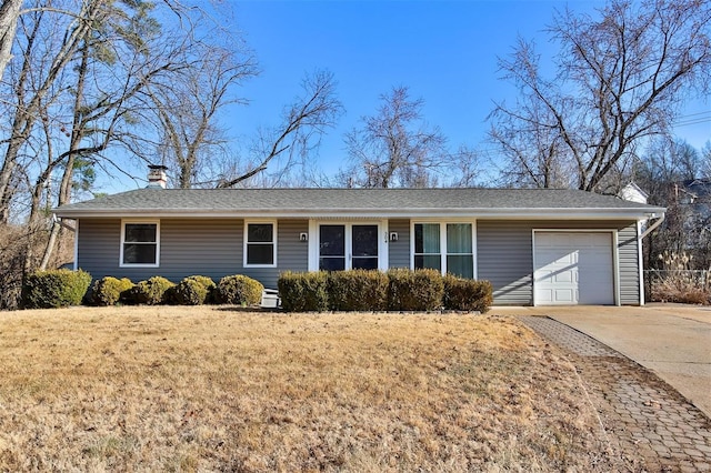 ranch-style home with a garage, a shingled roof, concrete driveway, a front lawn, and a chimney