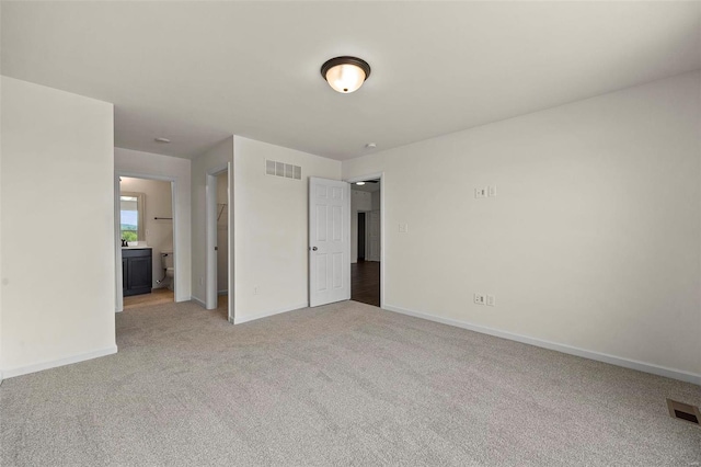 unfurnished bedroom featuring light carpet and ensuite bath