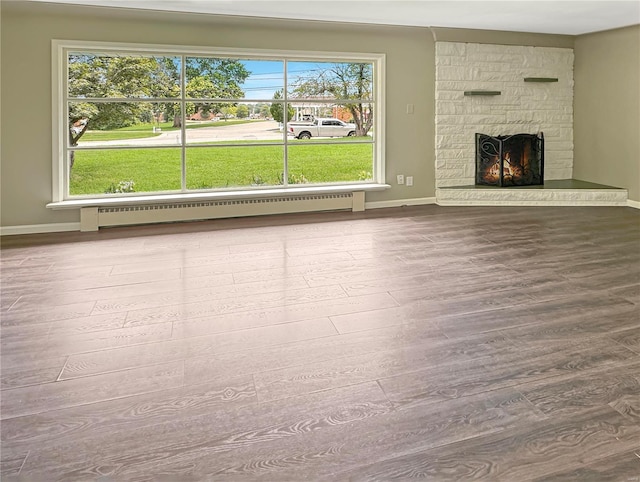 unfurnished living room featuring plenty of natural light, a stone fireplace, hardwood / wood-style flooring, and a baseboard radiator