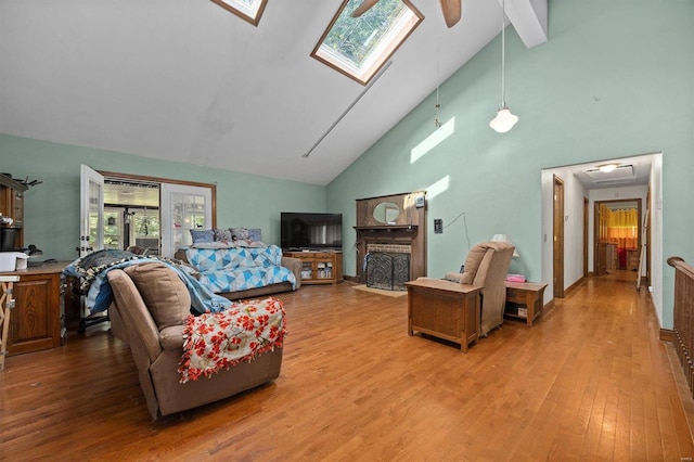 living room featuring ceiling fan, high vaulted ceiling, a skylight, and wood-type flooring