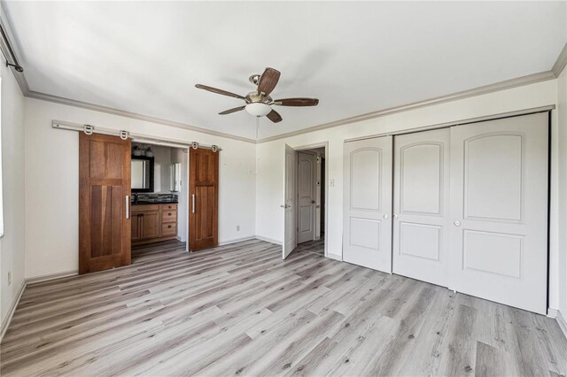 unfurnished bedroom featuring a closet, a barn door, crown molding, light wood-type flooring, and ceiling fan