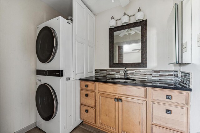 washroom featuring stacked washer and dryer, dark wood-type flooring, ceiling fan, cabinets, and sink